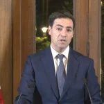 Imanol Pradales hablando en una reunión con fondo de banderas.