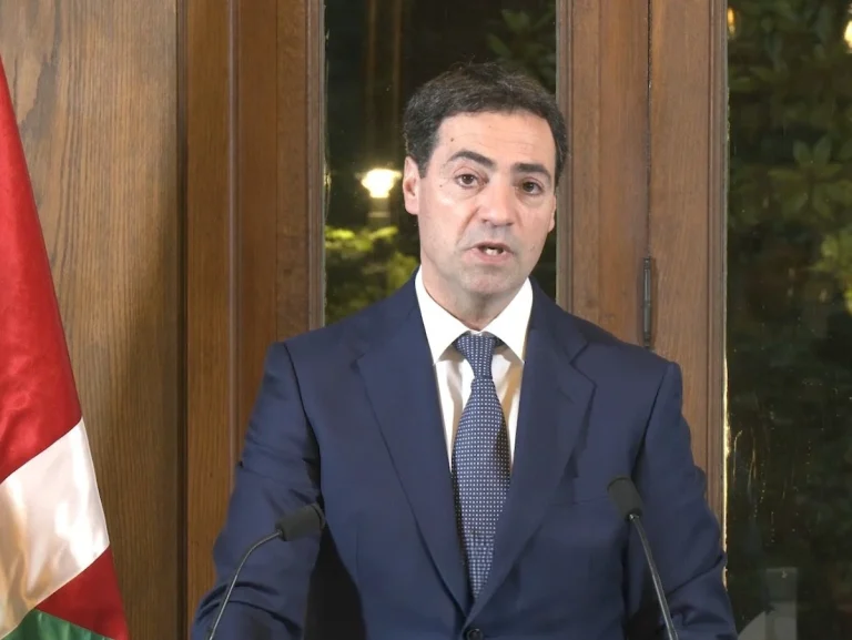 Imanol Pradales hablando en una reunión con fondo de banderas.