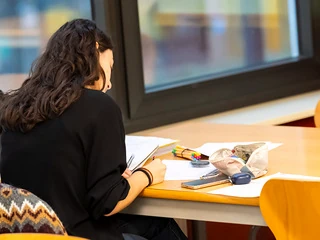 Estudiante escribiendo en una mesa de estudio con material escolar.