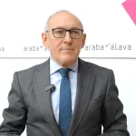 Hombre con traje y corbata frente a un fondo institucional.