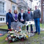 Grupo de personas junto a una ofrenda floral en un acto conmemorativo