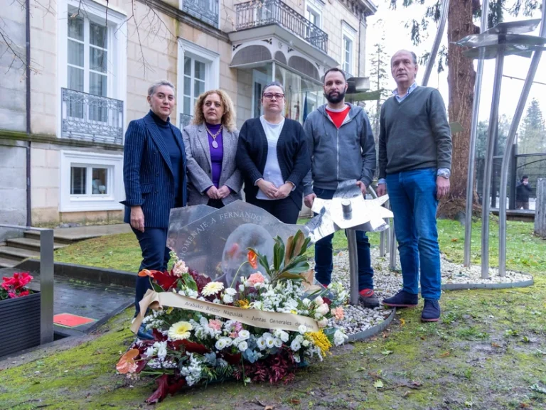 Grupo de personas junto a una ofrenda floral en un acto conmemorativo