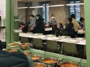 Comedores con platos de comida y personas en albergue juvenil
