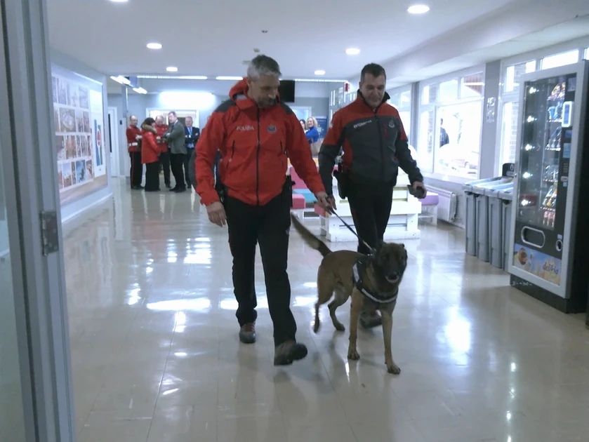 Dos hombres con chaquetas rojas caminan con un perro en un edificio