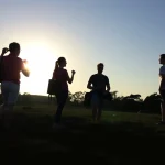 Siluetas de jóvenes conversando al atardecer en un campo.