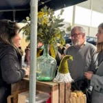 Tres personas conversando en un mercado con productos locales.