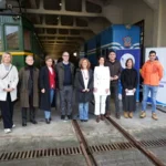 Grupo de personas posando frente a trenes en un taller ferroviario.
