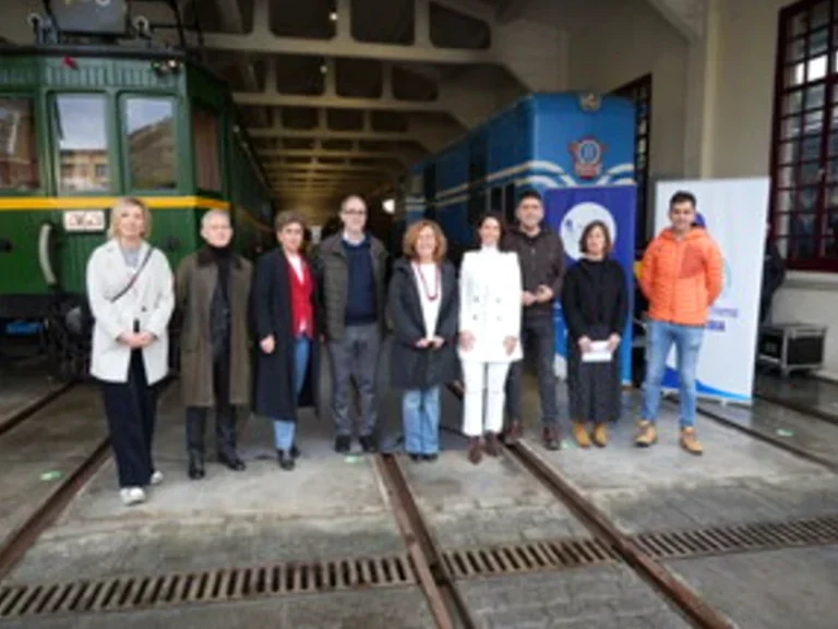 Grupo de personas posando frente a trenes en un taller ferroviario.