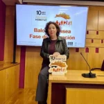 Mujer de pie junto a un cartel de Vitoria-Gasteiz Hobetuz en una sala de conferencias.