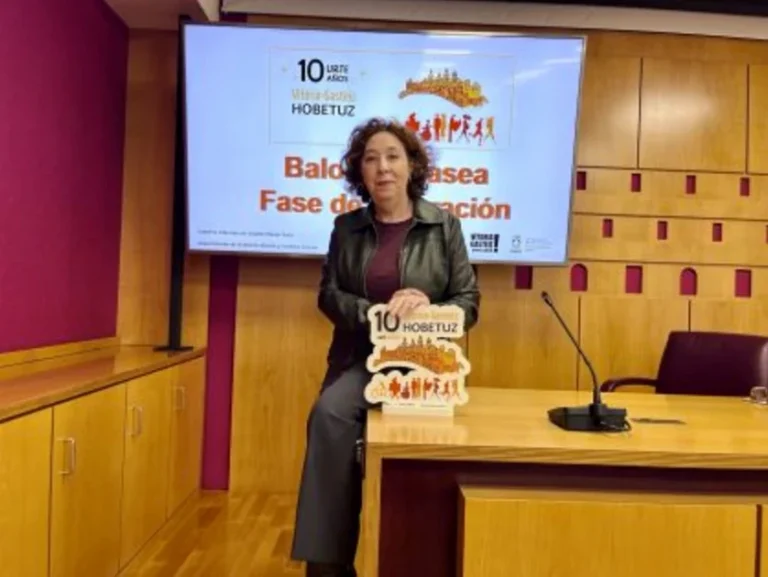 Mujer de pie junto a un cartel de Vitoria-Gasteiz Hobetuz en una sala de conferencias.