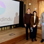 Tres personas posan frente a un logo de Berdindu en un evento