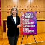 Mujer sonriente junto a cartel de conciertos en La Blanca 2026.