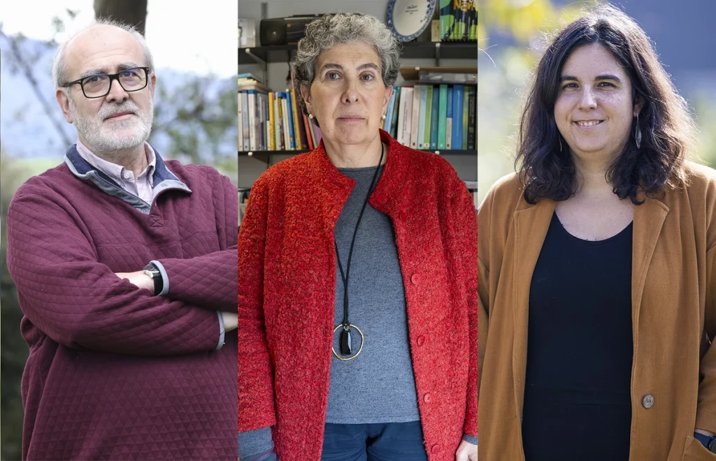 Tres personas de pie, una con suéter rojo, otra con abrigo marrón y una más con suéter gris.