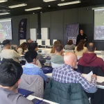 Sala de conferencias con asistentes escuchando a un ponente sobre fútbol femenino.