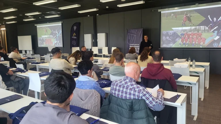 Sala de conferencias con asistentes escuchando a un ponente sobre fútbol femenino.