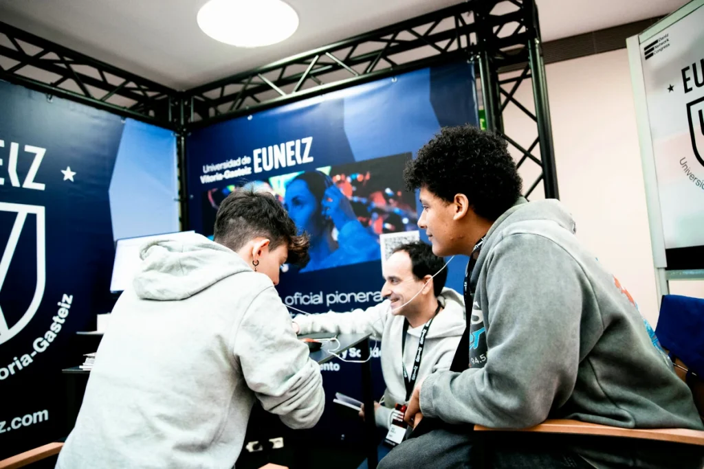 Tres personas conversando en el stand de EUNEIZ en un congreso