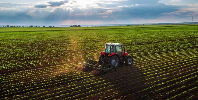 Tractor trabajando en un campo verde bajo un cielo nublado