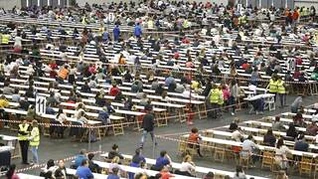 Gran cantidad de personas en un examen en un recinto amplio.
