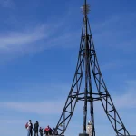 Grupo de personas junto a la cruz del Gorbea bajo un cielo azul