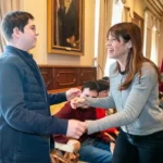 Dos personas sonrientes interactuando en un evento formal.