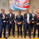 Cinco hombres de pie en un evento, fondo con pantallas