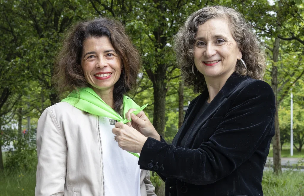 Dos personas en un entorno natural, una ajustando la ropa de la otra.