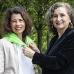 Dos personas en un entorno natural, una ajustando la ropa de la otra.