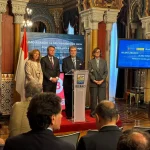 Cuatro personas en un evento oficial en Bilbao con pantallas informativas.