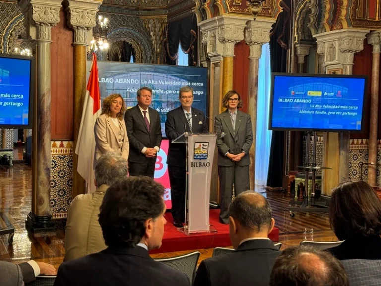 Cuatro personas en un evento oficial en Bilbao con pantallas informativas.