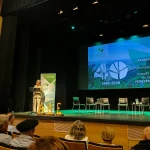 Escenario con presentadora y sillas vacías en evento forestal