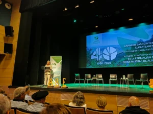 Escenario con presentadora y sillas vacías en evento forestal