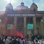 Edificio con humo rojo y personas en la manifestación del Primero de Mayo.