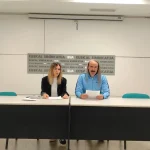 Dos personas sentadas en una mesa con documentos en mano.