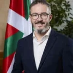 Hombre con barba y gafas frente a una bandera vasca.