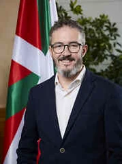 Hombre con barba y gafas frente a una bandera vasca.