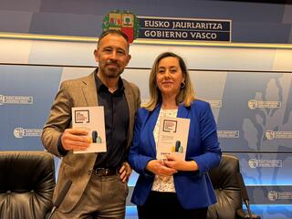 Dos personas sosteniendo documentos en un evento oficial del Gobierno Vasco.