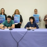 Grupo de personas sosteniendo carteles en una conferencia de prensa.
