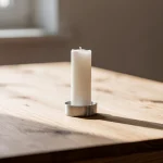 Vela blanca encendida sobre una mesa de madera clara.