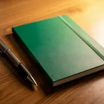 Cuaderno verde y bolígrafo sobre una mesa de madera