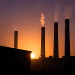 Silhouette de chimeneas industriales al atardecer con humo