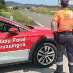 Un policía foral junto a un coche patrulla en una carretera