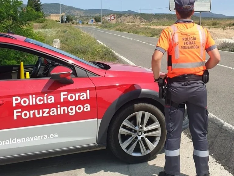 Un policía foral junto a un coche patrulla en una carretera