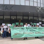 Protesta de auxiliares administrativos con pancartas frente a un edificio