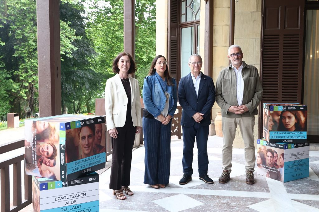 Cuatro personas posando junto a carteles de cursos de verano