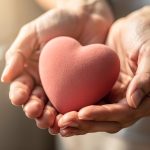 Manos sosteniendo un corazón de goma suave en color rosa.