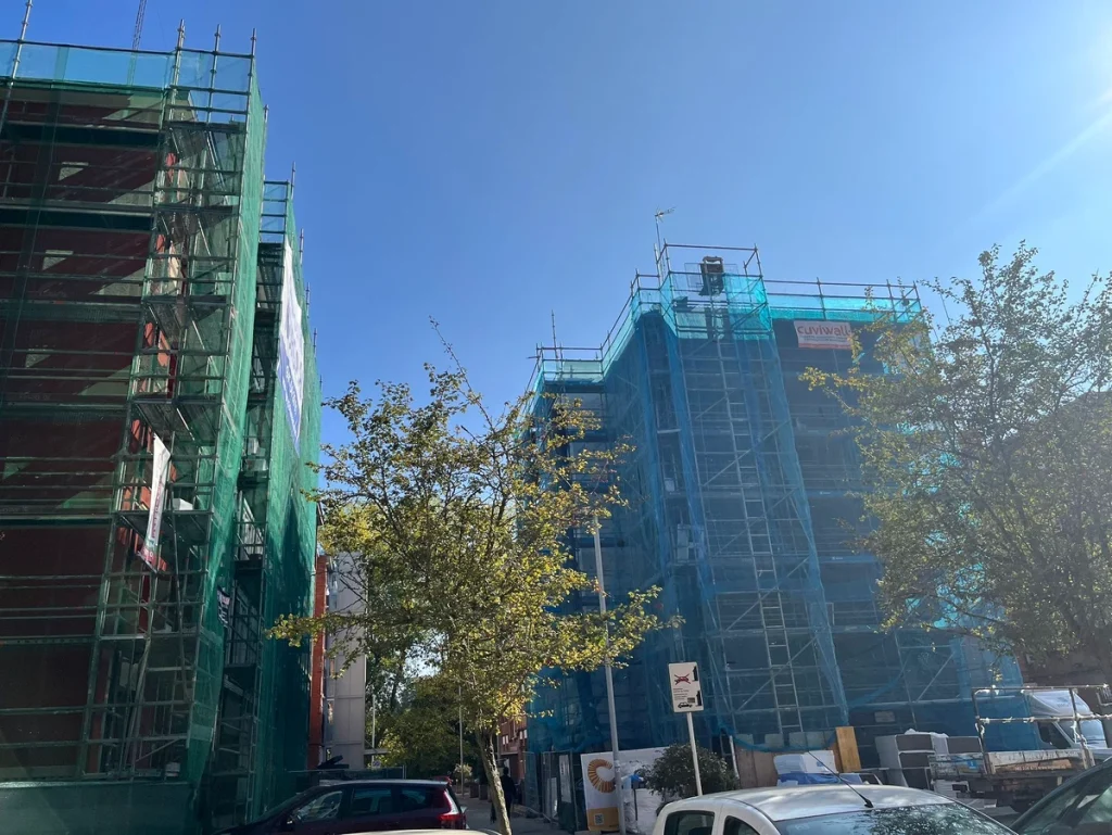 Edificios en rehabilitación con andamios y mallas verdes.