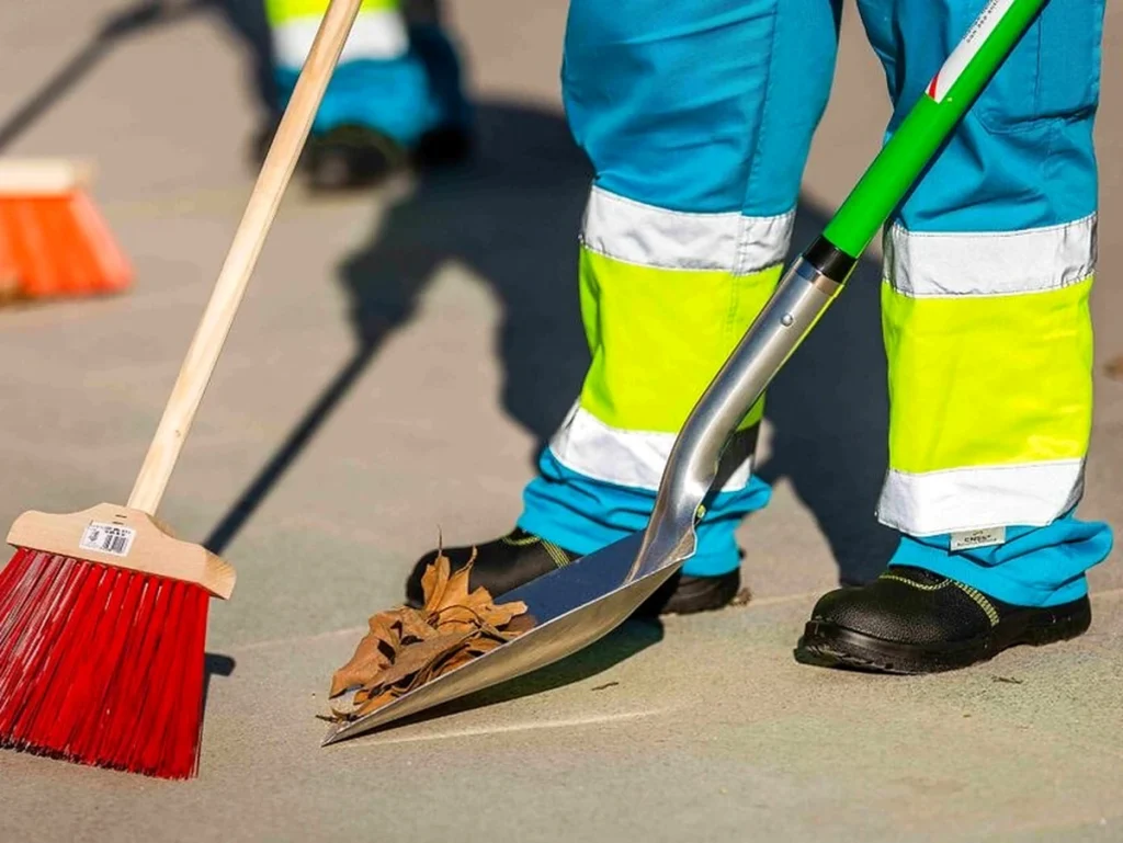 Trabajador de limpieza con escoba y pala en la calle
