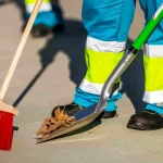 Trabajador de limpieza con escoba y pala en la calle