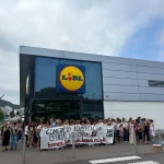 Grupo de personas protestando frente a un supermercado Lidl con pancarta.