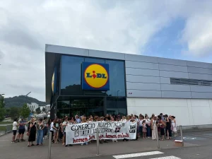 Grupo de personas protestando frente a un supermercado Lidl con pancarta.